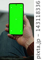 Man hand holding smartphone vertically with green screen chroma key and tracking markers over jeans. Close up view of male palm with isolated cellular template mockup inside office. Vertical photo. 143118336