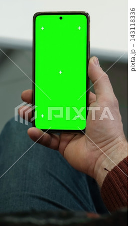 Man hand holding smartphone vertically with green screen chroma key and tracking markers over jeans. Close up view of male palm with isolated cellular template mockup inside office. Vertical photo. Man hand holding smartphone vertically with green screen chroma key and tracking markers over jeans. Close up view of male palm with isolated cellular template mockup inside office. Vertical photo. 143118336