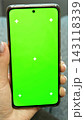 Female hand with neat manicure holding smart phone template mockup with clean green screen chroma key display and tracking crosses. Close up view of lady gadget tool isolated picture. Vertical photo. 143118339