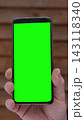 Close up of man dirty worker hand holding digital cellular phone template with isolated mockup green screen chroma key. Smartphone blank display near rustic wooden wall backdrop. Vertical shot. 143118340