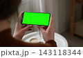 Girl sitting at home and watching movie on mobile phone template mockup with green screen chroma key. Female hands holding smartphone horizontally for digital entertainment leisure in cozy room 143118344