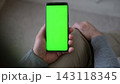Top view of man holding smartphone vertically with green screen mockup chroma key blank display. Male user sitting and looking at mobile phone template mockup surface inside cozy room at home 143118345