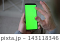 Top view of man hands holding smartphone vertically and gesturing on green screen mockup chroma key display. Male user tapping or zooming on mobile phone template mockup surface inside cozy room 143118346