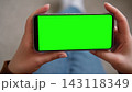 Top view of woman hands holding smartphone horizontally with green screen mockup chroma key blank display. Female user looking at phone template mockup screen for video streaming or mobile gaming 143118349