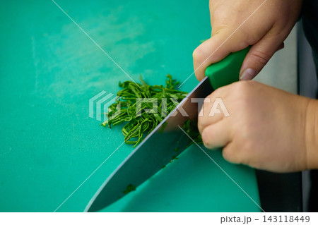 Cook finely chopping fresh herbs on cutting board in professional restaurant kitchen Cook finely chopping fresh herbs on cutting board in professional restaurant kitchen 143118449