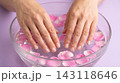 Close-up of a woman's hands soaking in a clear glass bowl of warm water with pink flower petals for a relaxing manicure prep. 143118646