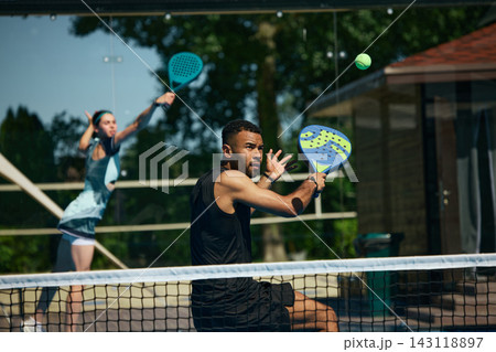 Male padel athlete executing fast volley near net with female partner covering court 143118897