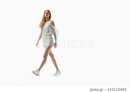 Young woman walking confidently in casual white outfit on studio background 143118982