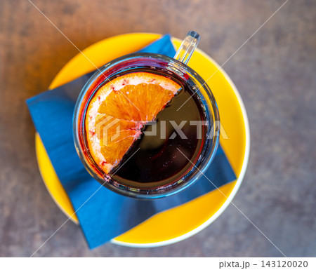 Top view of a warm cup of mulled wine with a half orange slice floating on the surface, placed on a rustic wooden table during winter. Top view of a warm cup of mulled wine with a half orange slice floating on the surface, placed on a rustic wooden table during winter. 143120020