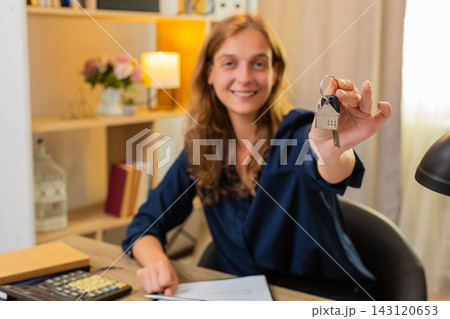 Young woman on home table showing house keys to camera and celebrating new home rental success joy Young woman on home table showing house keys to camera and celebrating new home rental success joy 143120653