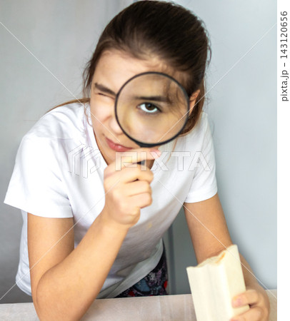Curious girl examining a book with a magnifying glass in a playful moment of study and discovery 143120656