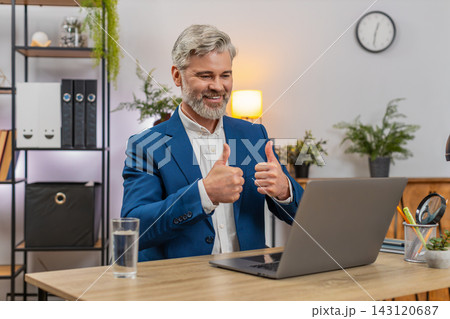 Middle-aged businessman enjoys laptop news views soaring sales raises thumbs up celebrating success Middle-aged businessman enjoys laptop news views soaring sales raises thumbs up celebrating success 143120687