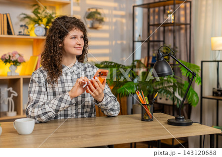 Young woman on home table texting on smartphone with smile after good message about meeting or job Young woman on home table texting on smartphone with smile after good message about meeting or job 143120688