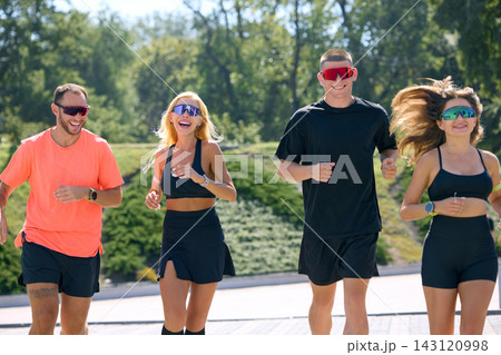 Group of athletic friends jogging together outdoors in sunny city park Group of athletic friends jogging together outdoors in sunny city park 143120998