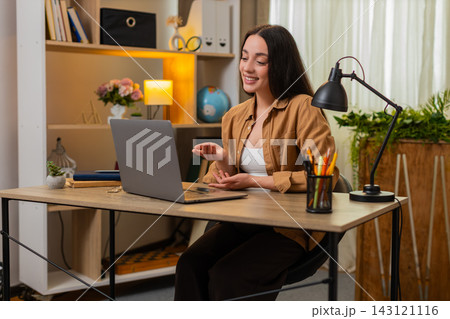 Young woman on home table attending online meeting listening carefully and answering with confidence Young woman on home table attending online meeting listening carefully and answering with confidence 143121116
