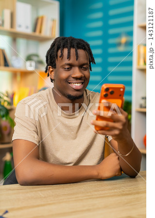 African American young man on home table reading smartphone message and smiling with good news joy 143121187