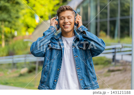 Young man listening to music on headphones walking in city street with happy relaxed smile outdoors 143121188