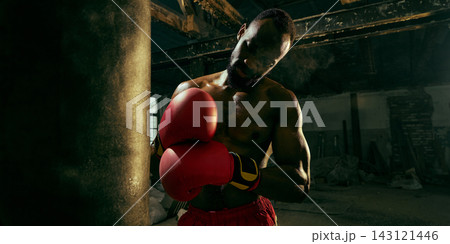 Professional boxer lowers his gloves beside a heavy bag with exhausted resilience 143121446