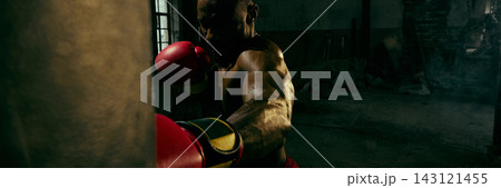 Powerful boxer strikes a heavy bag in a dark industrial gym with fierce determination 143121455