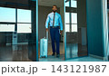 Businessman walks through airport entrance pulling a suitcase with composed determination 143121987