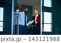 Male manager gestures while discussing travel plans with female colleague near airport entrance with confident focus 143121988