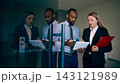 Corporate colleagues review a tablet and documents beside glass doors in airport with productive concentration 143121989