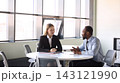 Two business travelers discuss a project at a table in bright airport lounge with cooperative focus 143121990