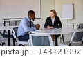 Businesswoman interviews a male professional at a table in airport meeting room with focused attention 143121992
