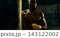 Sweaty athlete pauses beside a punching bag with determined exhaustion 143122002