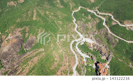 Horizontal aerial view of winding mountain serpentine road and monastery building among unique rock formations and green hills in Meteora Greece Horizontal aerial view of winding mountain serpentine road and monastery building among unique rock formations and green hills in Meteora Greece 143122216