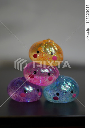 Four colorful glitter-filled sensory toys are stacked into a small pyramid against a softly blurred neutral background. The image represents balance, playful creativity, cooperation, and the joy of Four colorful glitter-filled sensory toys are stacked into a small pyramid against a softly blurred neutral background. The image represents balance, playful creativity, cooperation, and the joy of 143123013