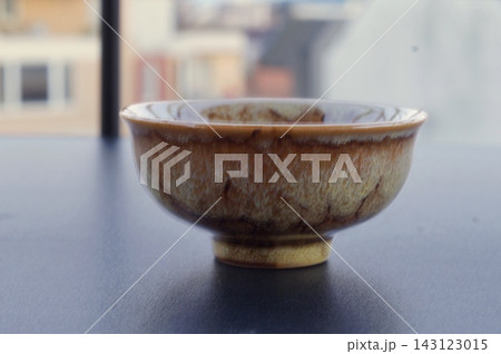 Rustic handcrafted ceramic tea bowl with mottled brown glaze is displayed on a dark tabletop in soft natural light. The image symbolizes artisanal craftsmanship, imperfect beauty, and mindful everyday Rustic handcrafted ceramic tea bowl with mottled brown glaze is displayed on a dark tabletop in soft natural light. The image symbolizes artisanal craftsmanship, imperfect beauty, and mindful everyday 143123015