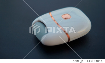 A white and blue wireless computer mouse with rose gold details rests diagonally on a dark background. The minimalist electronic accessory represents modern design, mobility, and efficient digital 143123054