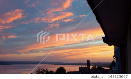 Vivid pink and orange sunset clouds stretch above a calm sea, with a dark building edge framing the right side. The image conveys tranquility, transition, and the beauty of evening light. Vivid pink and orange sunset clouds stretch above a calm sea, with a dark building edge framing the right side. The image conveys tranquility, transition, and the beauty of evening light. 143123067