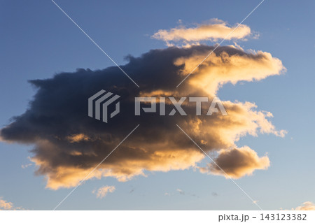 Sculptural golden cloud glowing above blue evening sky with dramatic shadow Sculptural golden cloud glowing above blue evening sky with dramatic shadow 143123382