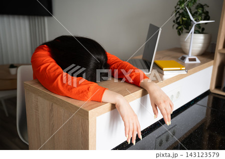 Woman resting her head on a home office desk beside laptop and study materials. Remote work fatigue burnout awareness and online study overload Woman resting her head on a home office desk beside laptop and study materials. Remote work fatigue burnout awareness and online study overload 143123579