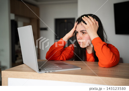 Frustrated woman holding her head while using laptop at desk in home office. Workplace stress technology frustration and deadline anxiety Frustrated woman holding her head while using laptop at desk in home office. Workplace stress technology frustration and deadline anxiety 143123580