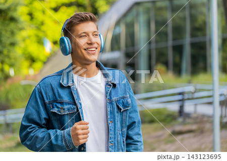 Young man enjoying music with headphones and smiling while walking in city street outdoors in town 143123695