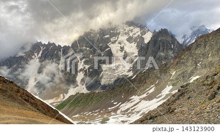 Clouds cross Ushba slopes, wide shot over snowfields and rocky passes in Svaneti, Georgia, presenting trekking terrain 143123900