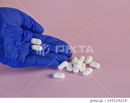 Medication Handling Concept - Blue Gloved Hand Holding White Tablets On Pink Background Medication Handling Concept - Blue Gloved Hand Holding White Tablets On Pink Background 143124214