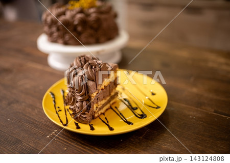 Chocolate layer cake slice on yellow plate with chocolate drizzle in warm cafe lighting Chocolate layer cake slice on yellow plate with chocolate drizzle in warm cafe lighting 143124808