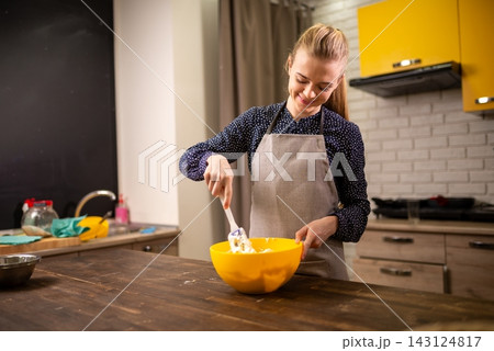 Woman stirring batter in yellow bowl on wooden counter in modern kitchen with matching 143124817