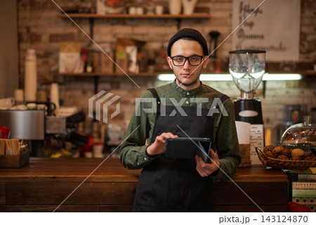 An young male barista using a digital tablet at a cafe counter An young male barista using a digital tablet at a cafe counter 143124870