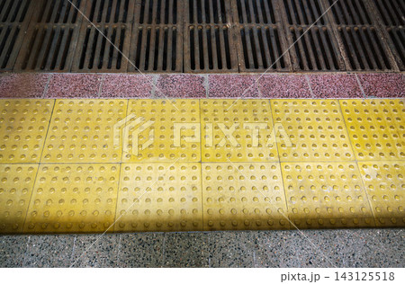 Top view of yellow tactile paving tiles with drainage grid providing barrier free environment for visually impaired 143125518