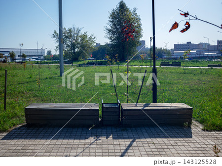 Modern backless wooden benches with central litter bin on stone tile pavement in public city park for outdoor relaxation 143125528