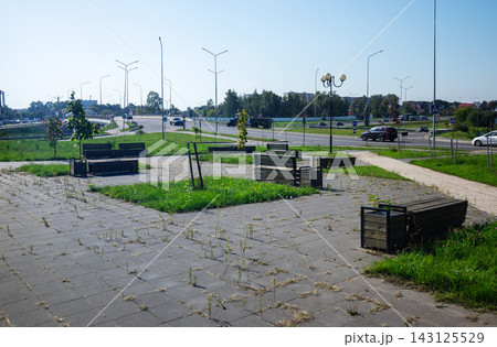 Modern public rest area with wooden benches on paved square next to city highway under blue sky for urban infrastructure Modern public rest area with wooden benches on paved square next to city highway under blue sky for urban infrastructure 143125529
