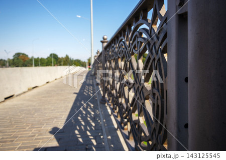 Geometric shadows cast from ornate metal fence on paved city bridge walkway in bright sunlight with copy space Geometric shadows cast from ornate metal fence on paved city bridge walkway in bright sunlight with copy space 143125545