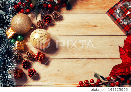 Rustic Christmas background featuring a frame of gifts, gold ornaments, pine cones, red berries, and decorations on a wooden table, with ample copy space. Rustic Christmas background featuring a frame of gifts, gold ornaments, pine cones, red berries, and decorations on a wooden table, with ample copy space. 143125996