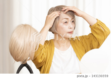 薄毛に悩みウイッグをつけるシニア女性 143130359