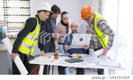 A group of workers have gathered around the architect's desk and are looking at a laptop. The process of discussing project details. Team building 143131103